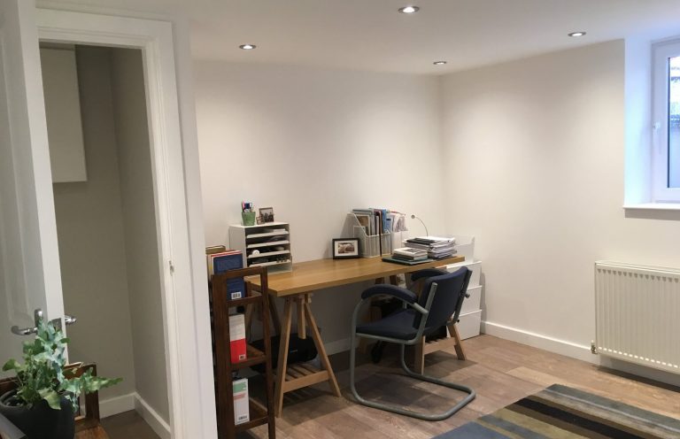 A minimalist home office with a desk, chair, printer, and indoor plants.